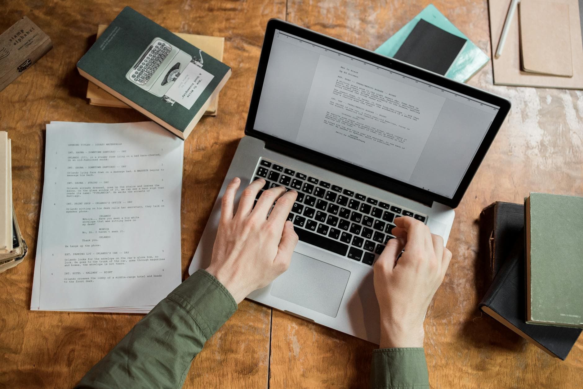 Faceless creator's hands typing on a laptop with script pages, suggesting content strategy and workflow.
