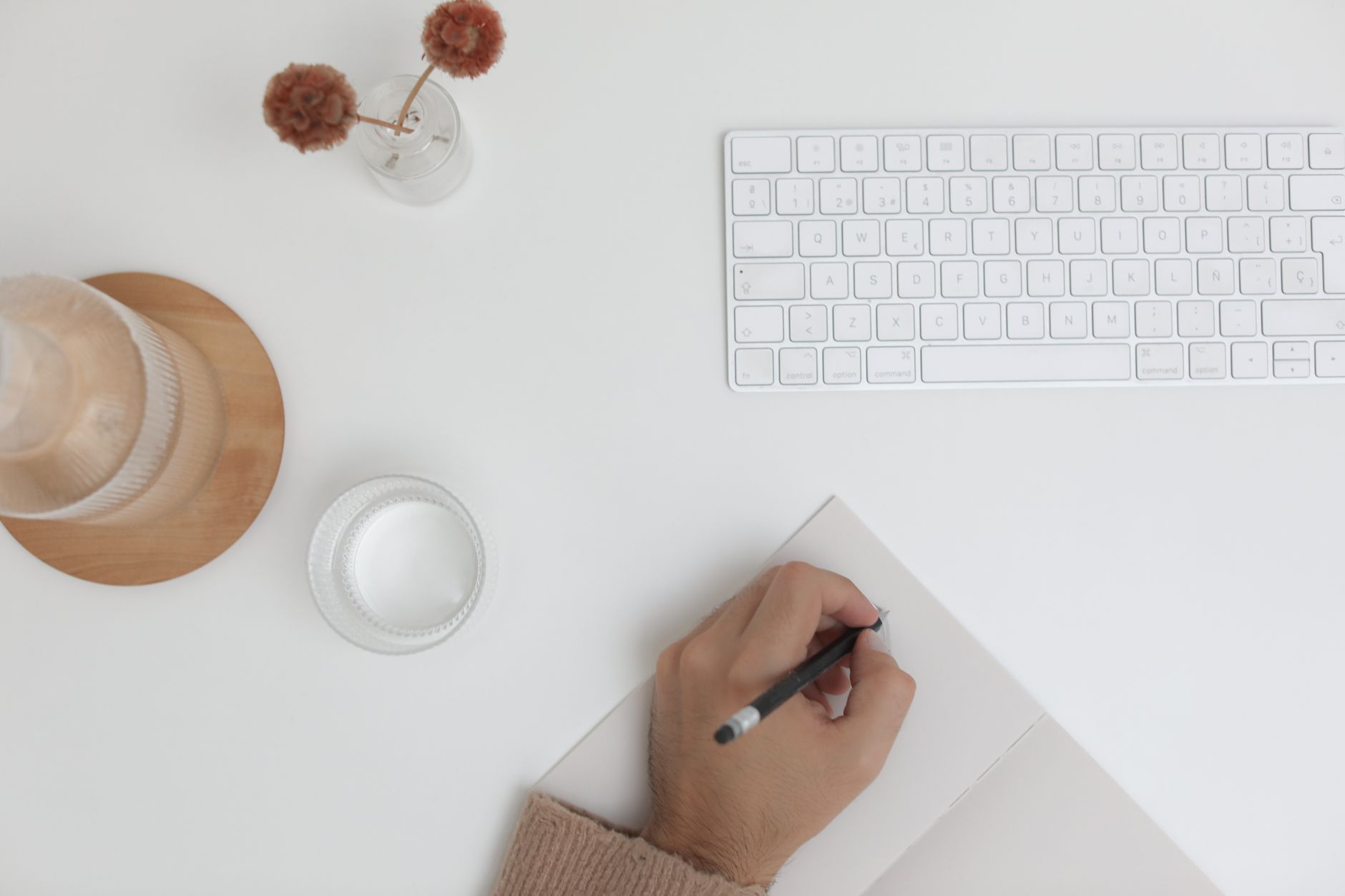 Faceless YouTube creator's hand writing in a notebook next to a keyboard and glass of water.