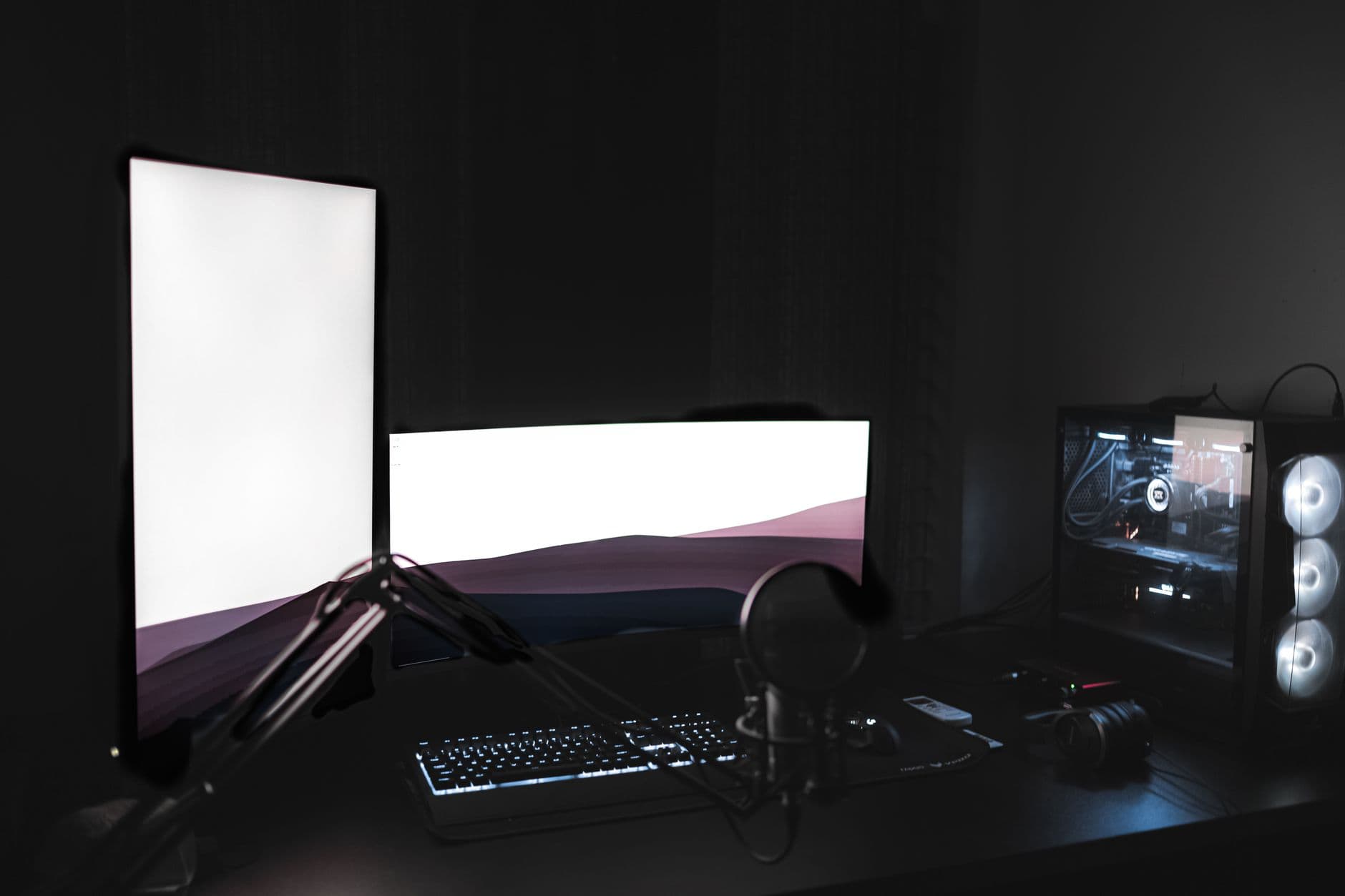 Faceless YouTube creator's desk setup with dual monitors, keyboard, and microphone for content creation.