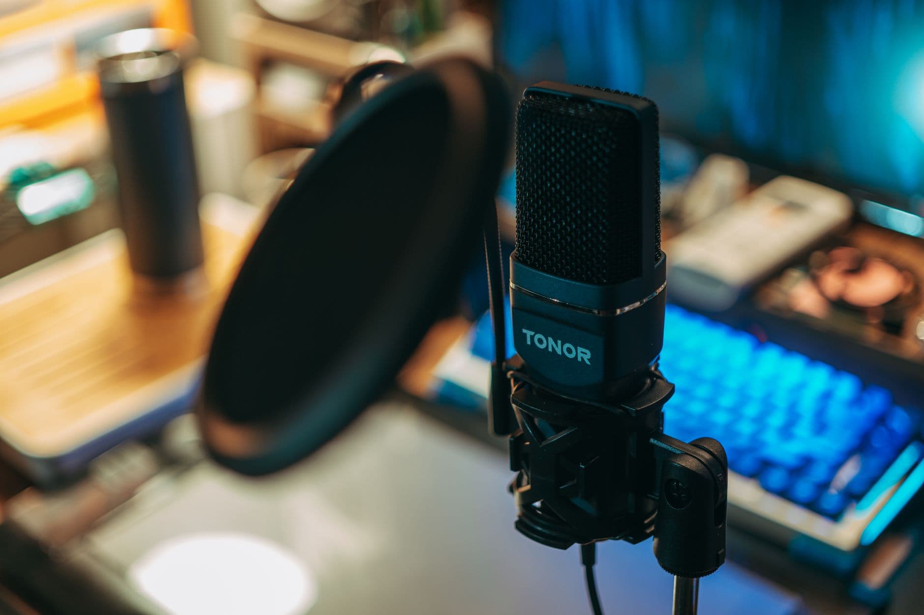 Close-up of a TONOR microphone and pop filter on a desk with a glowing keyboard, suggesting a faceless YouTube creator workspace.