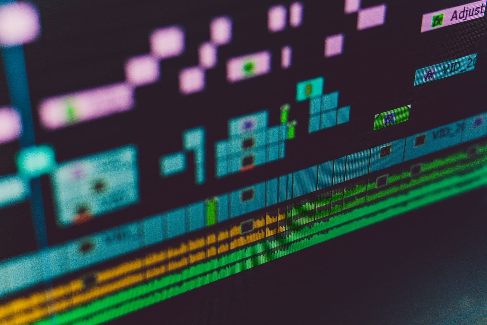 Close-up of a video editing timeline on a computer monitor, showing audio waveforms and video clips for content creation.