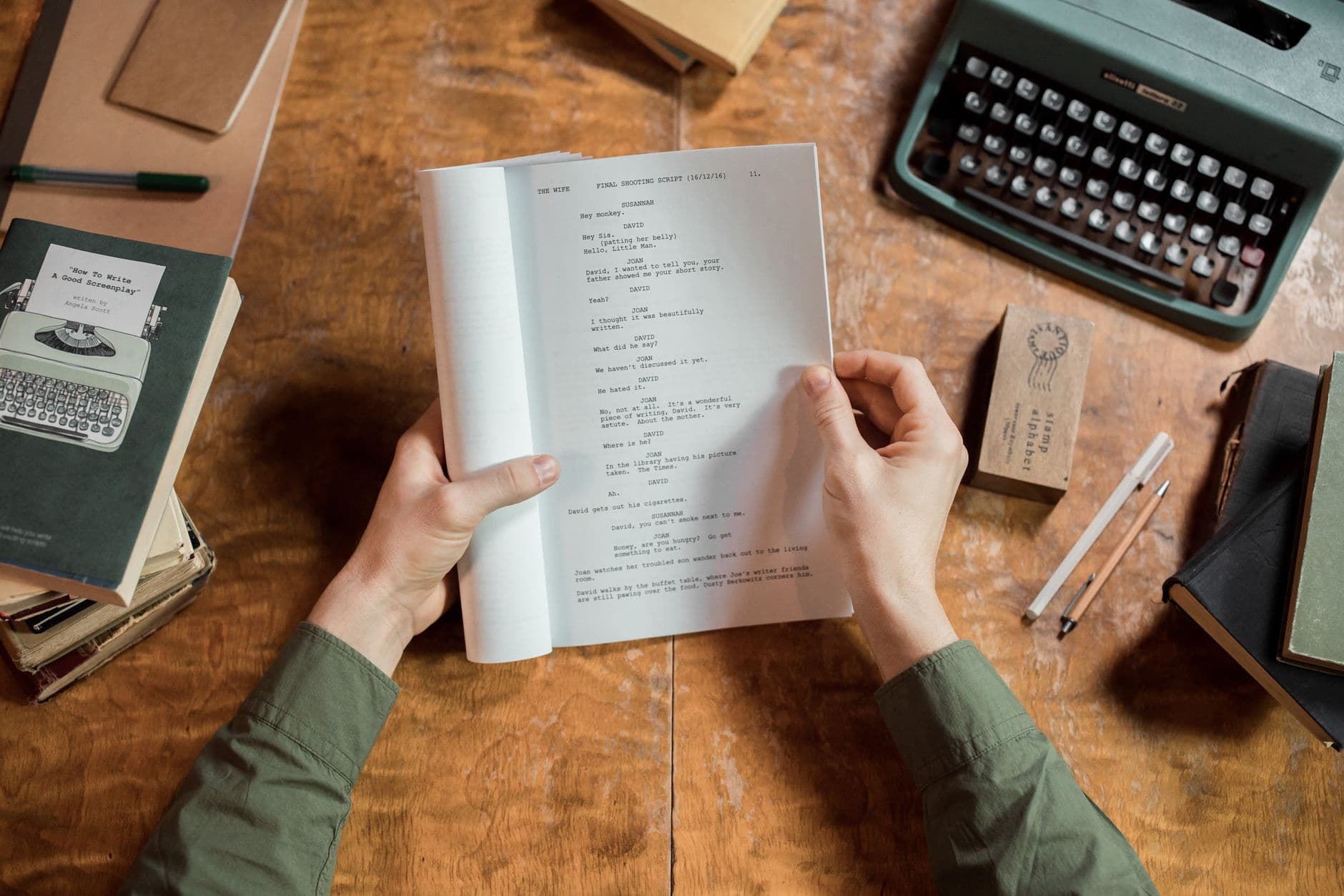 Hands holding a script for a faceless YouTube creator, surrounded by writing tools and books.