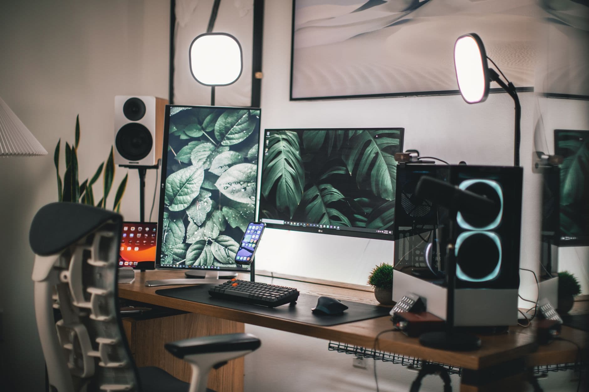 A clean desk setup with dual monitors displaying nature imagery, a PC tower, and studio lighting for content creation.