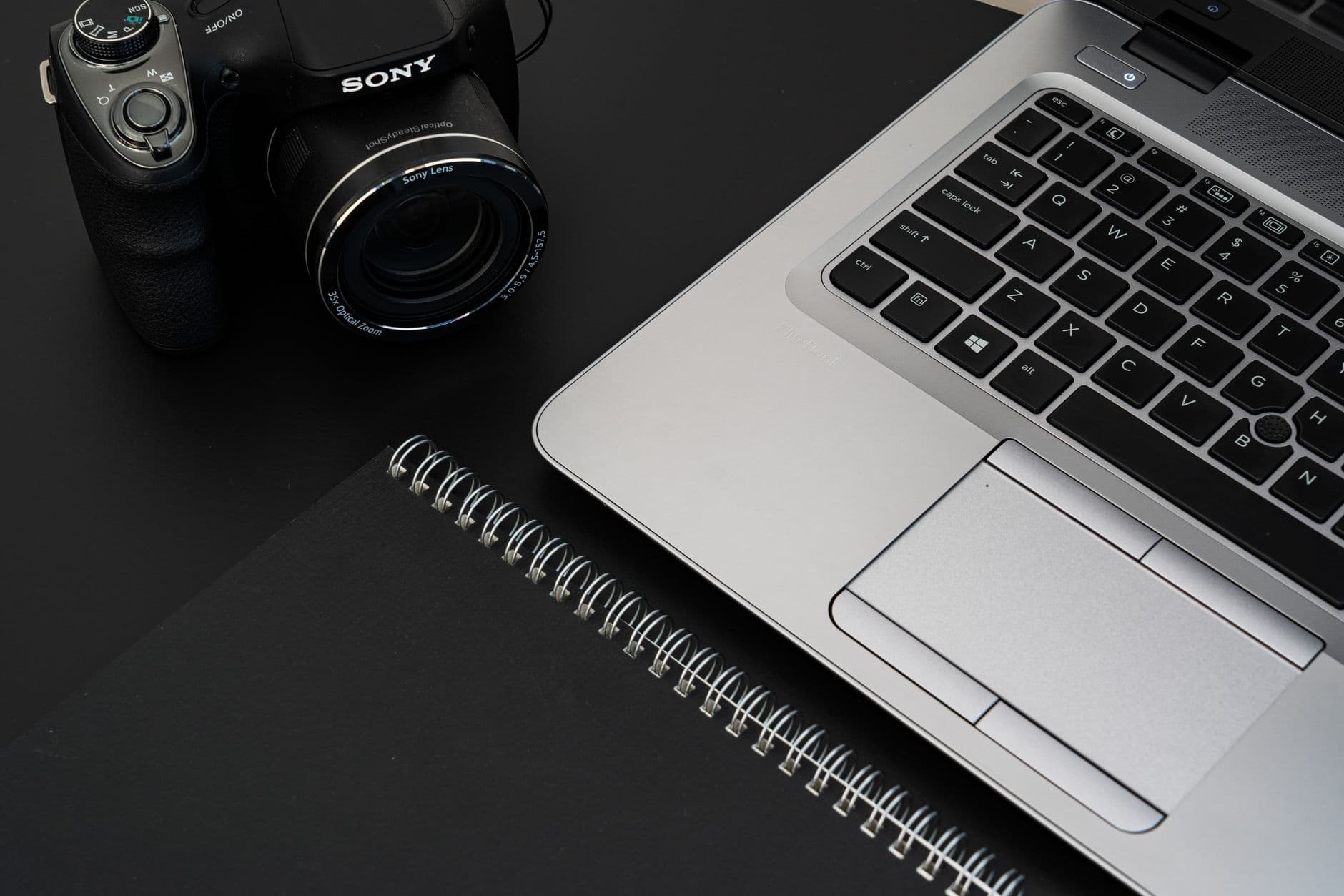 Faceless YouTube creator's camera, laptop, and notebook for content planning and workflow adaptation.