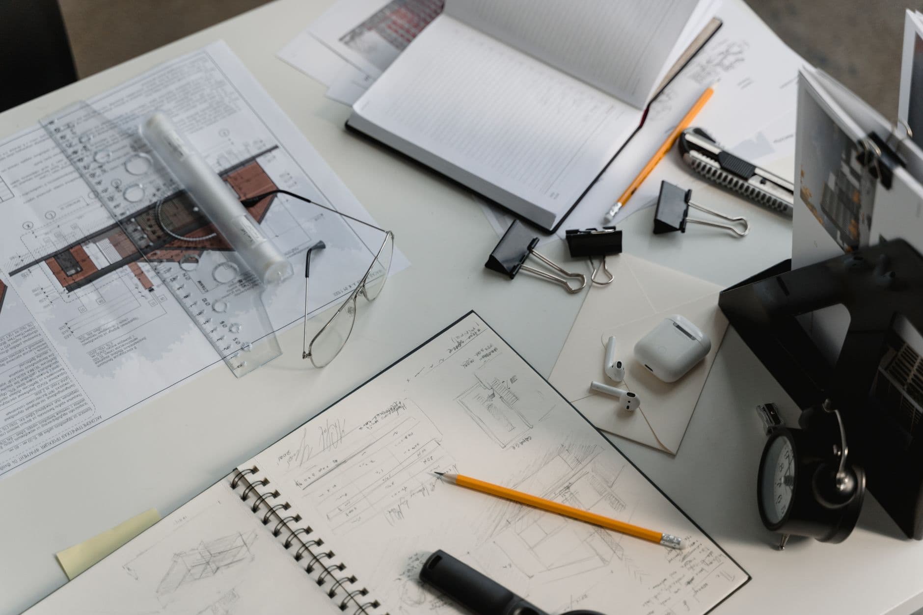 Faceless YouTube creator's planning desk with blueprints, notebooks, and AirPods for content strategy.