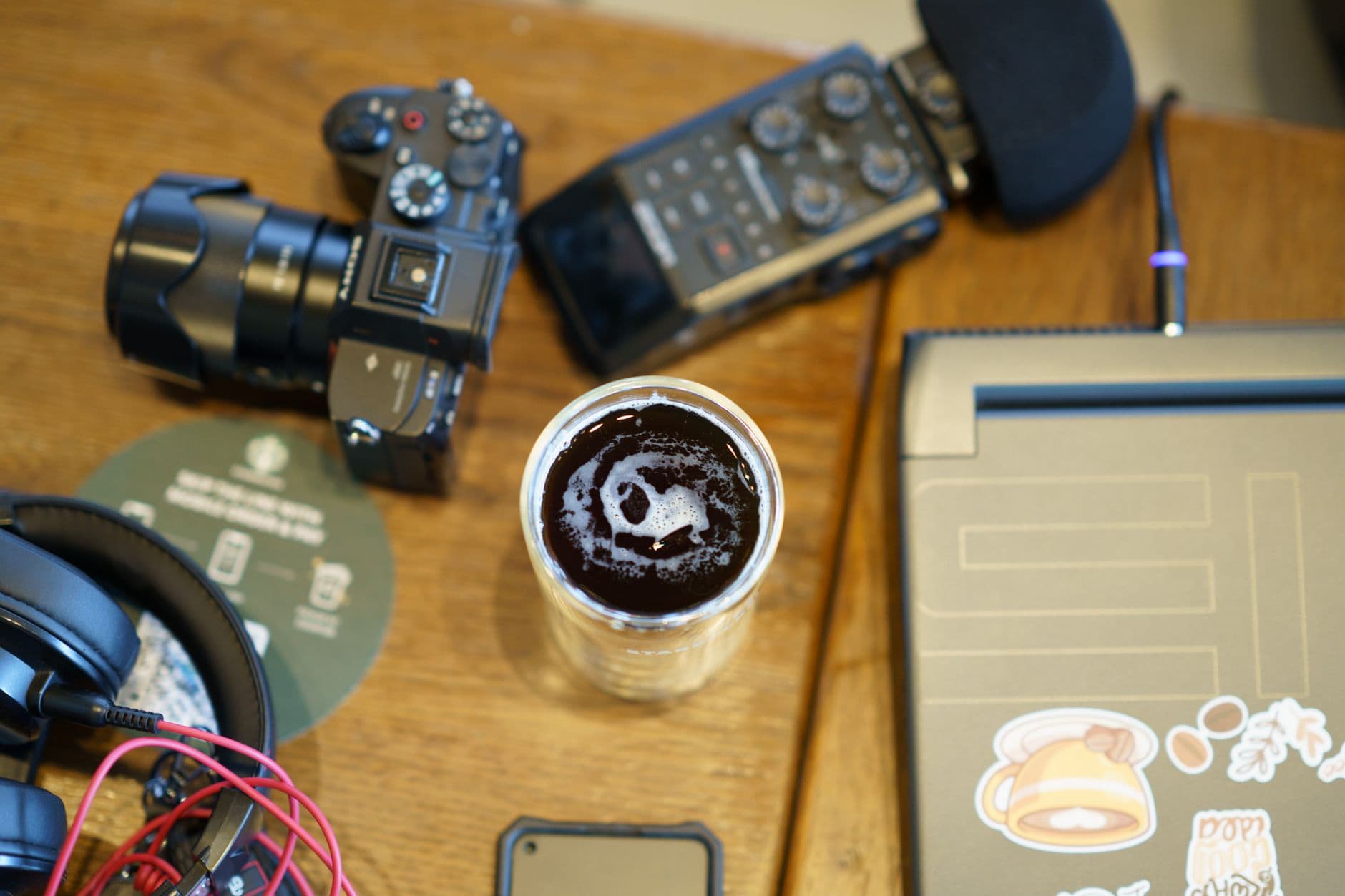 Faceless creator's desk with camera, recorder, headphones, and coffee for AI tool auditing.