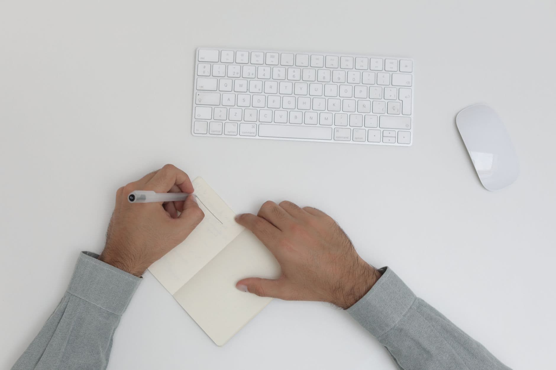 Faceless YouTube creator's hands writing in a notebook with a keyboard and mouse nearby.