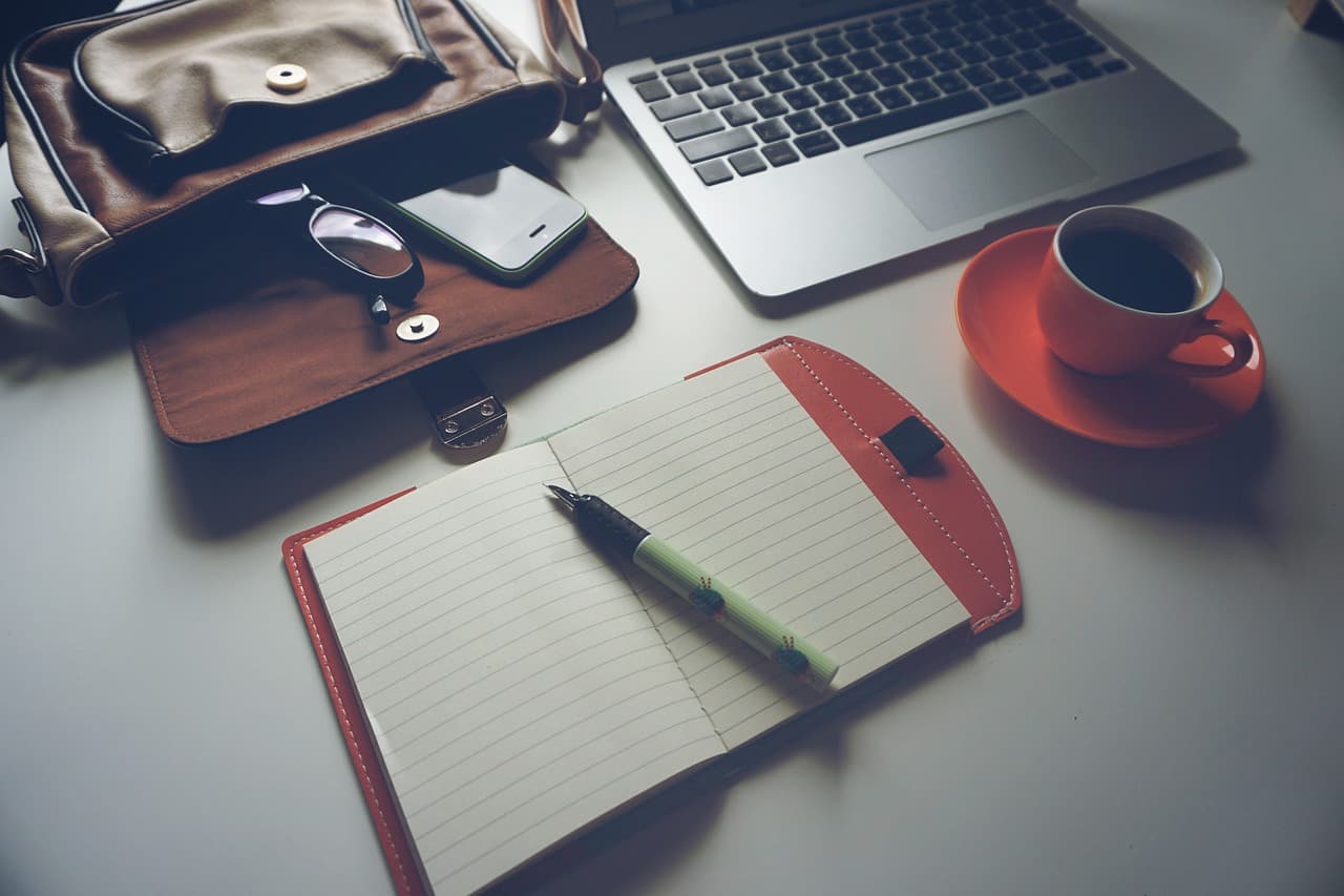 Faceless YouTube creator's desk with laptop, notebook, and coffee for scriptwriting.