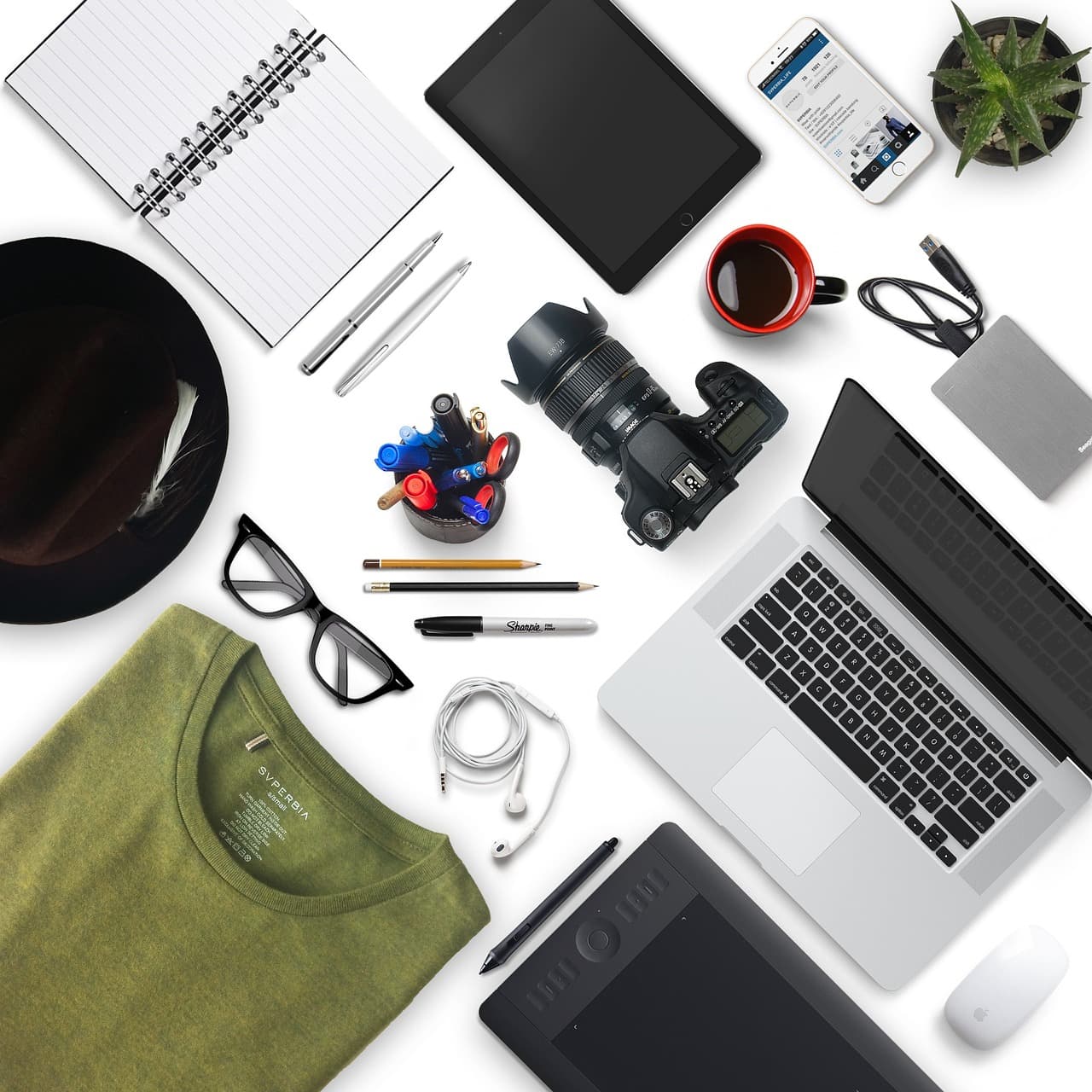 Flat lay of creator tools including camera, laptop, tablet, and notebook for faceless YouTube channel planning.
