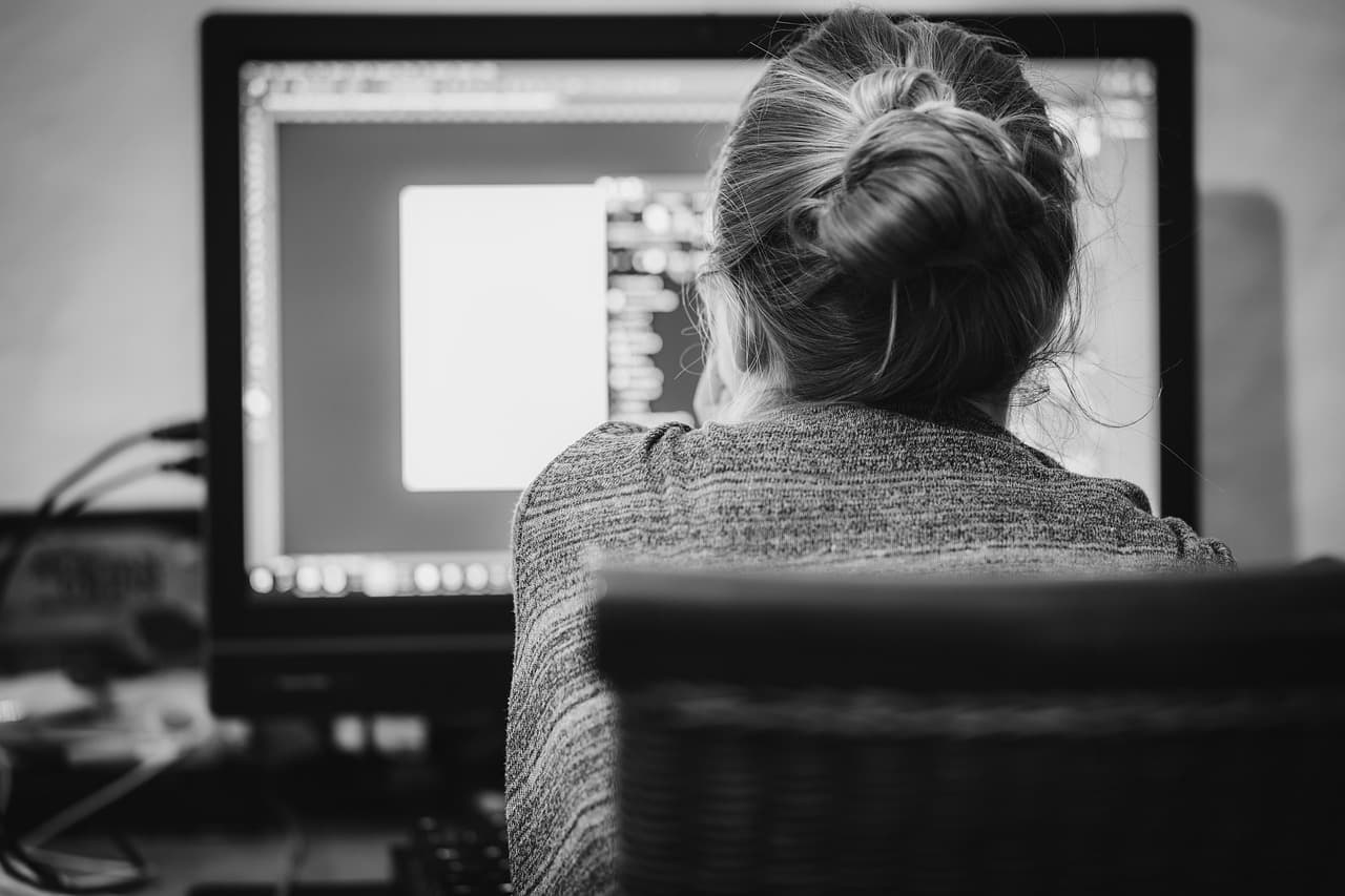 Faceless creator's back as they work on a computer, editing content for a YouTube workflow.