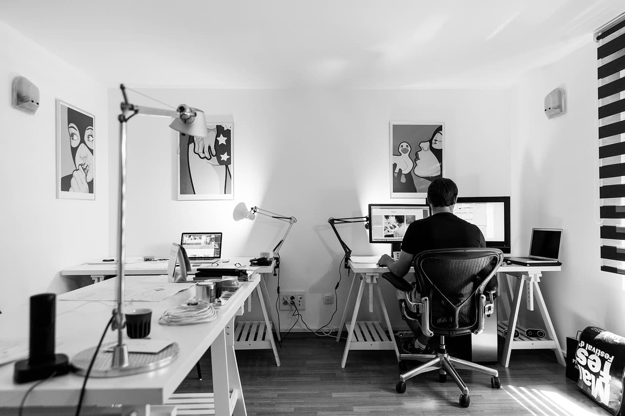 Faceless creator's workspace with multiple desks, laptops, and monitors for AI workflow planning.