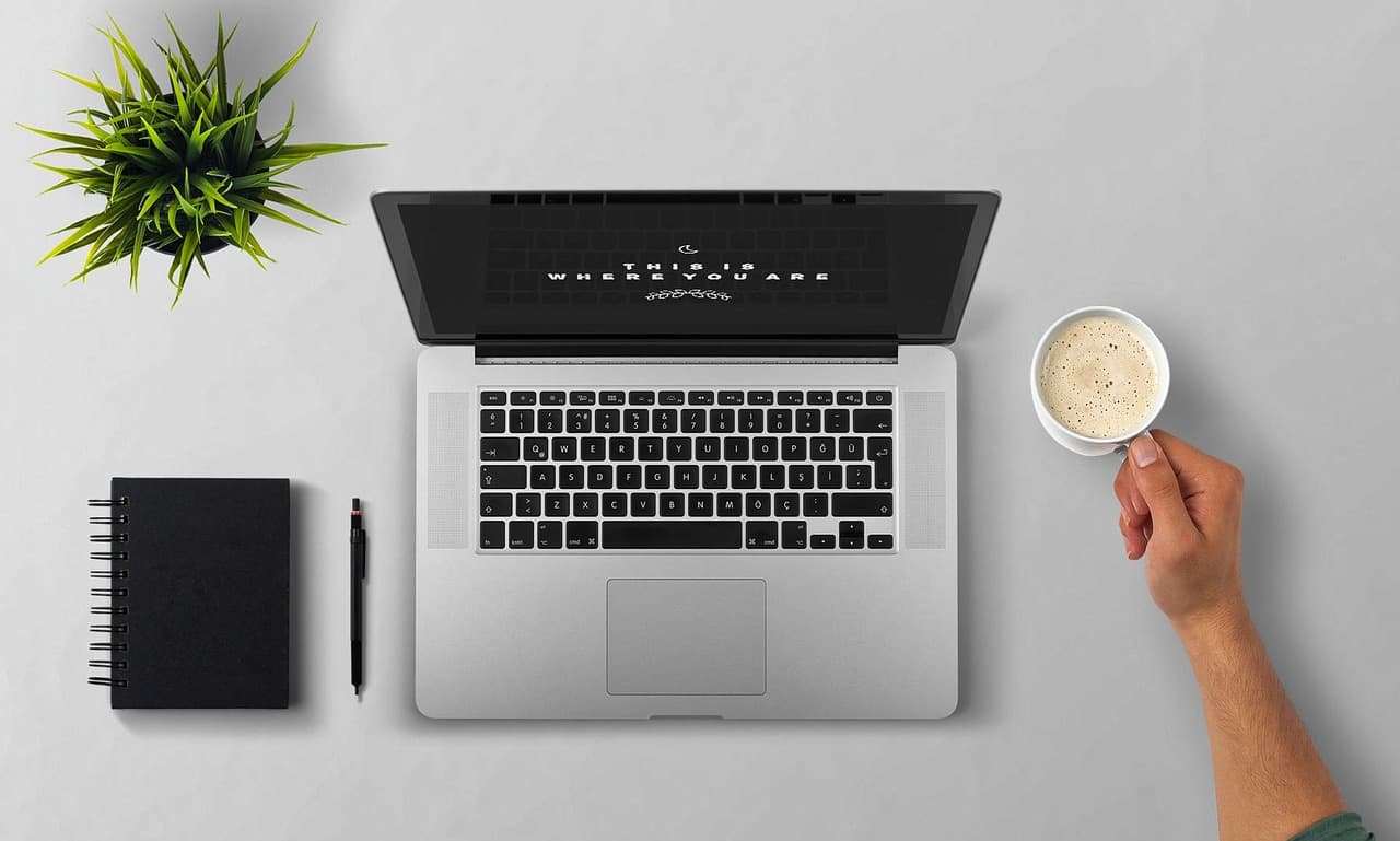 Faceless creator's workspace with laptop, notebook, and coffee for AI content workflow management.