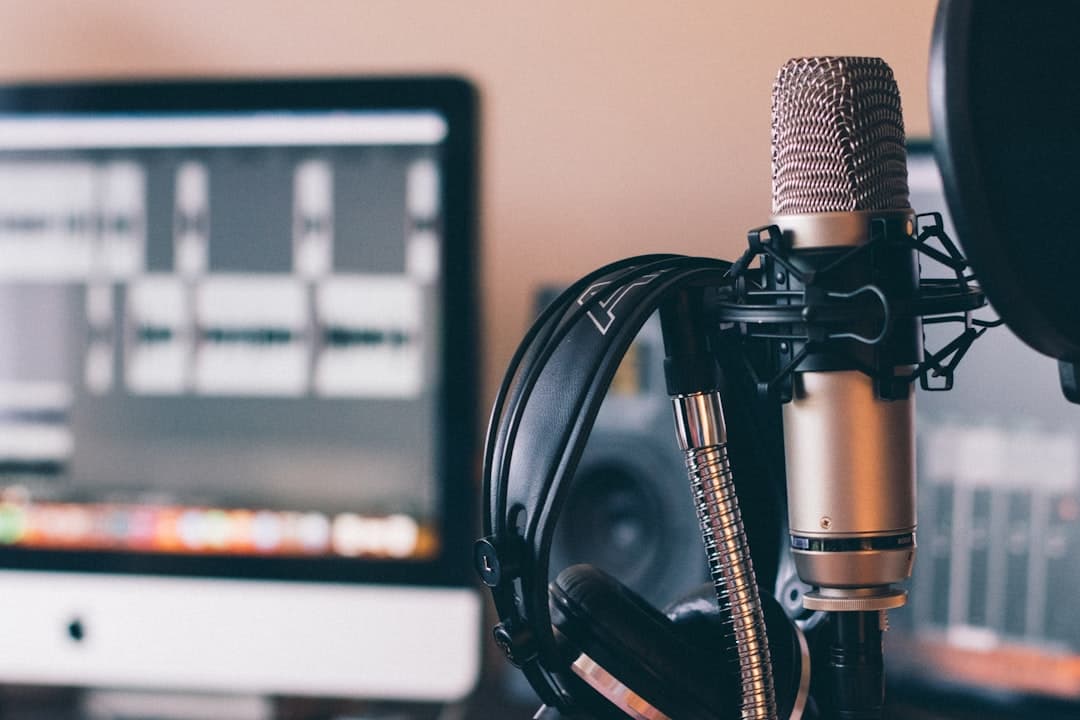 Faceless YouTube creator's studio setup with microphone, headphones, and computer monitor displaying audio editing software.
