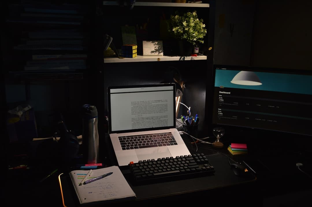 Faceless YouTube creator's desk with laptop showing text and monitor displaying a dashboard.