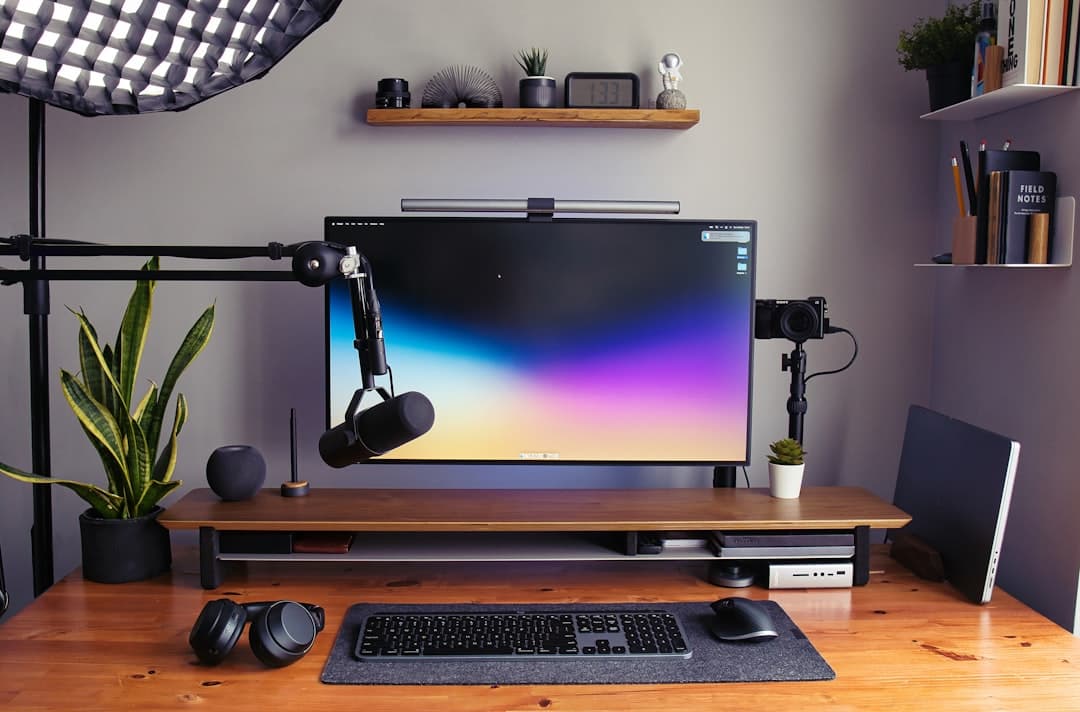 Faceless YouTube creator's desk with microphone, camera, and monitor displaying a colorful gradient.