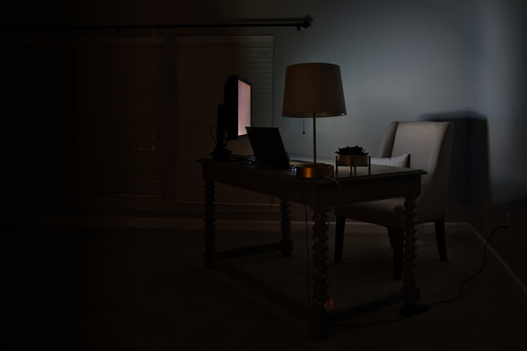 Faceless YouTube creator's desk with laptop and monitor in a dimly lit room, suggesting research and content creation.