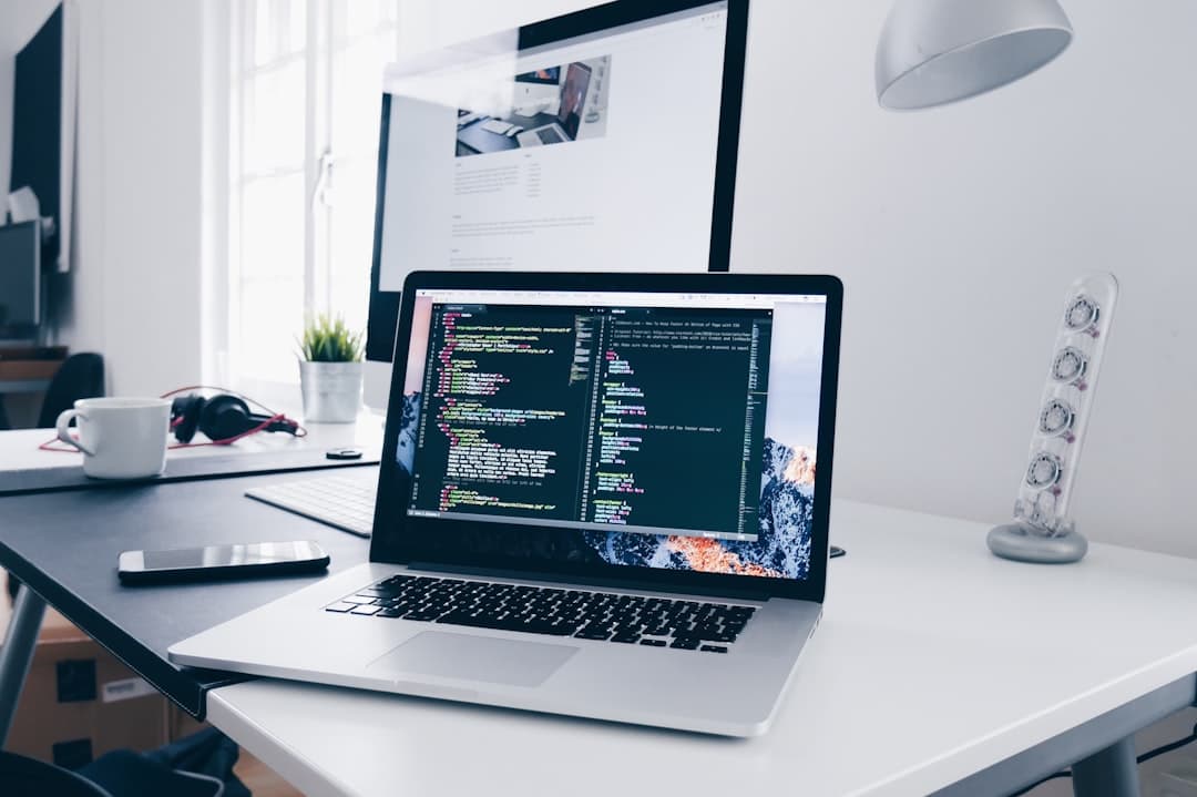 Faceless YouTube creator's desk with laptop displaying code and dual monitors for workflow.