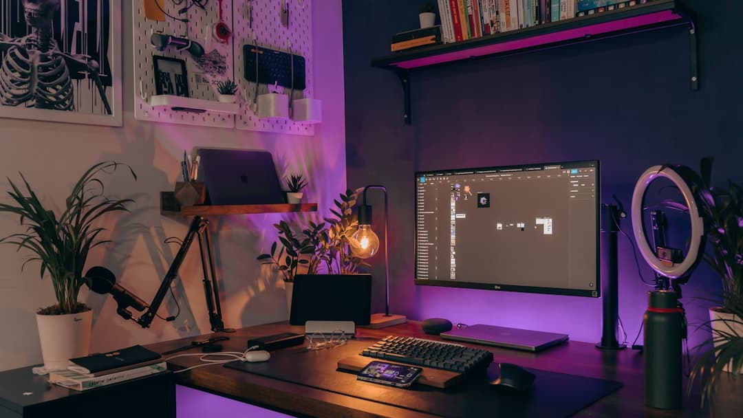 Faceless YouTube creator's desk setup with laptop, monitor showing video editing timeline, and microphone.