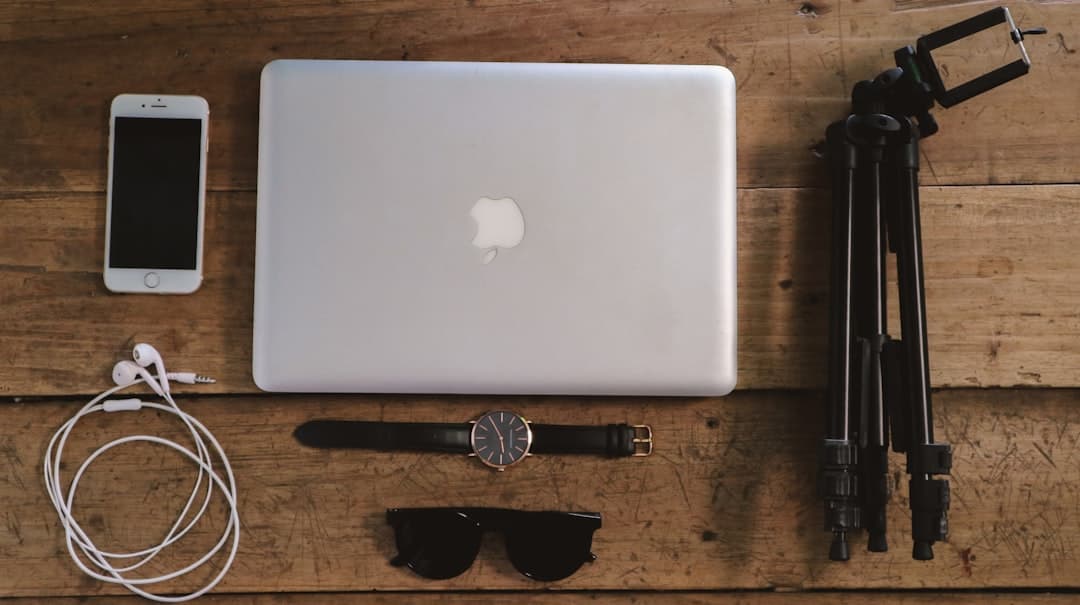 Faceless YouTube creator's workspace with laptop, smartphone, headphones, and tripod.