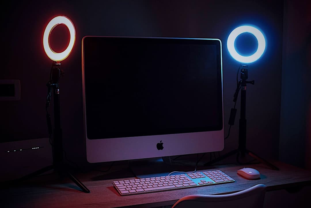 Faceless YouTube creator's desk setup with dual monitors, ring lights, and keyboard.