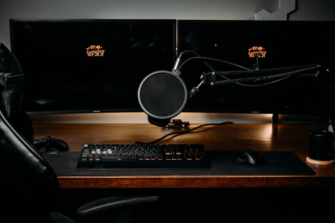 Faceless YouTube creator's dual monitor setup with keyboard, mouse, and microphone for content production.
