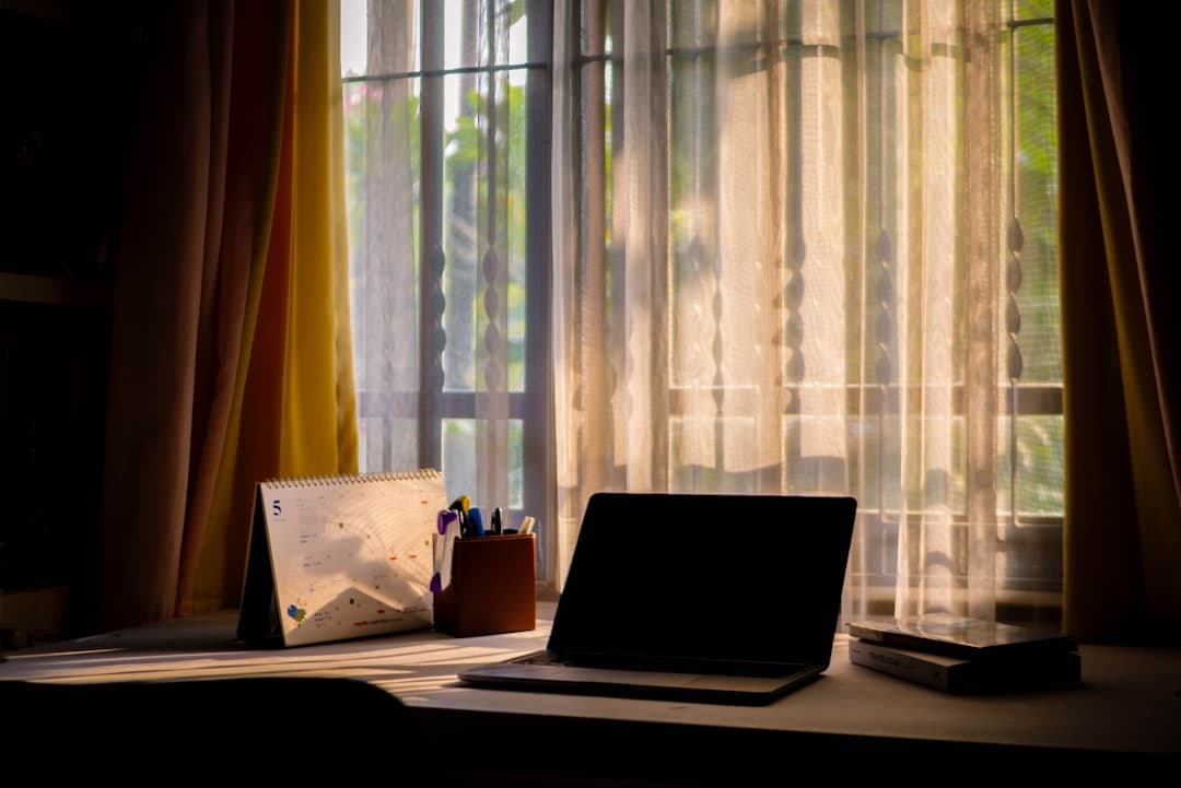 Faceless YouTube creator's desk with laptop, calendar, and pens, bathed in sunlight.