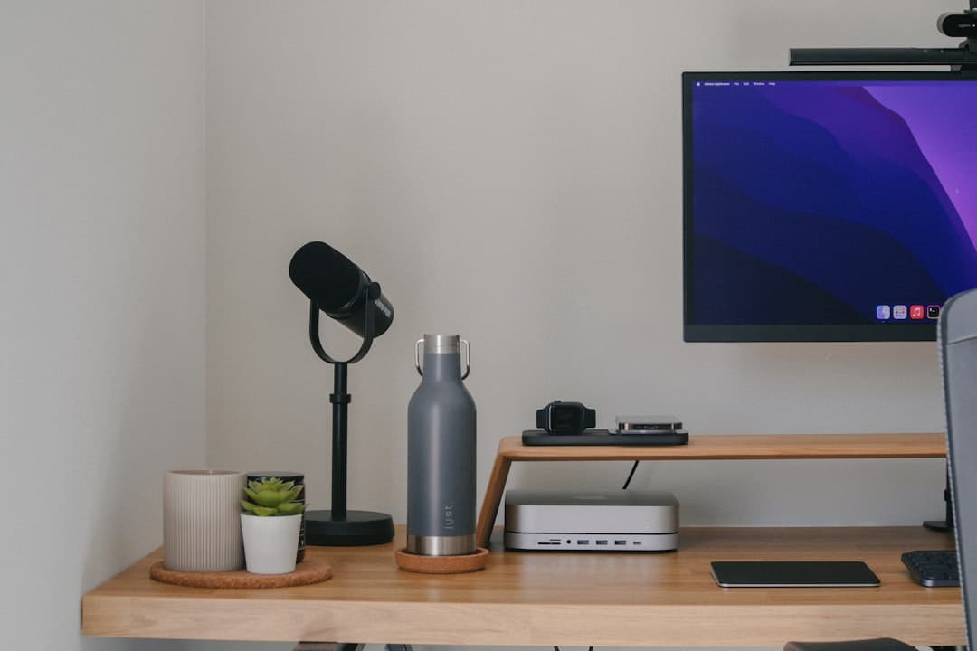 Faceless YouTube creator's desk setup with microphone, computer monitor, and water bottle.