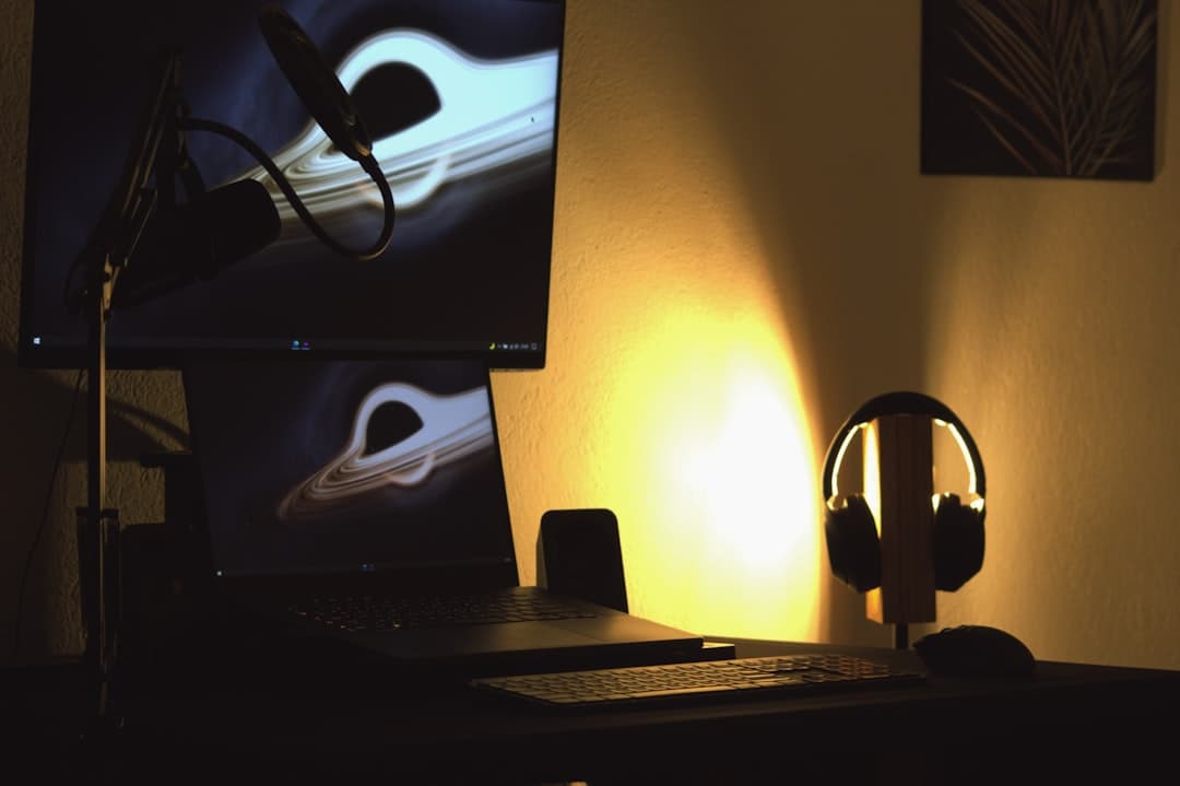 Faceless YouTube creator's desk setup with microphone, headphones, and monitor displaying abstract art.