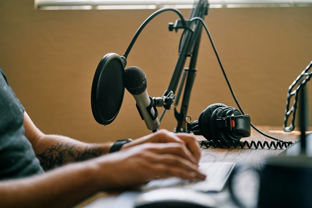 Faceless YouTube creator's hands typing on a keyboard with a microphone and headphones on the desk.