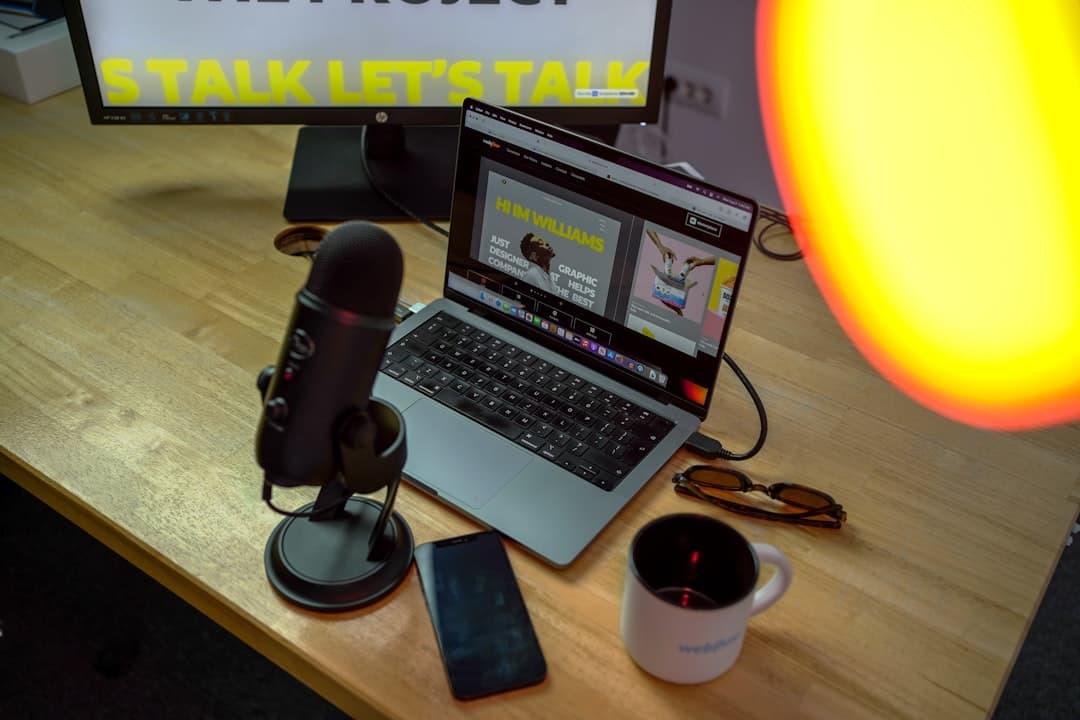 Faceless YouTube creator's desk setup with microphone, laptop, and monitor showing a website.