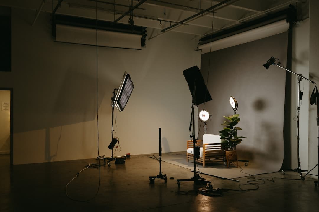 A dimly lit studio with multiple lighting rigs, a chair, and a plant, set up for video production.