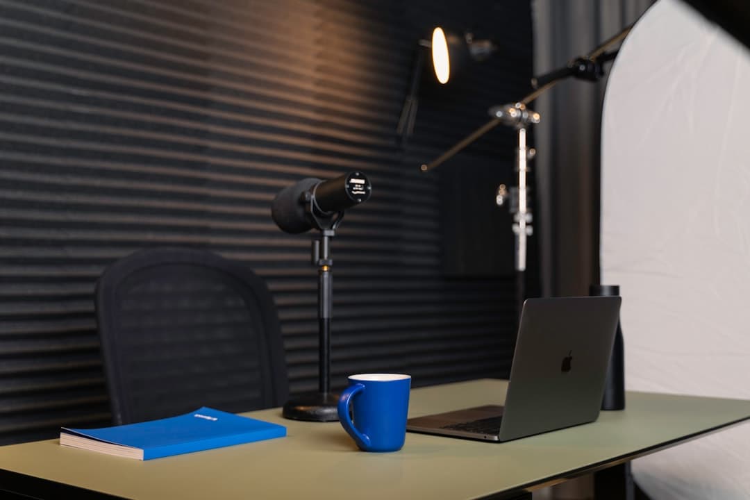 Faceless YouTube creator's desk with laptop, microphone, and notebook for video production planning.