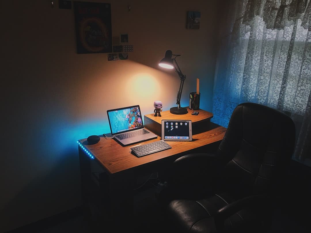 Faceless YouTube creator's desk with laptop, tablet, and keyboard for content strategy.