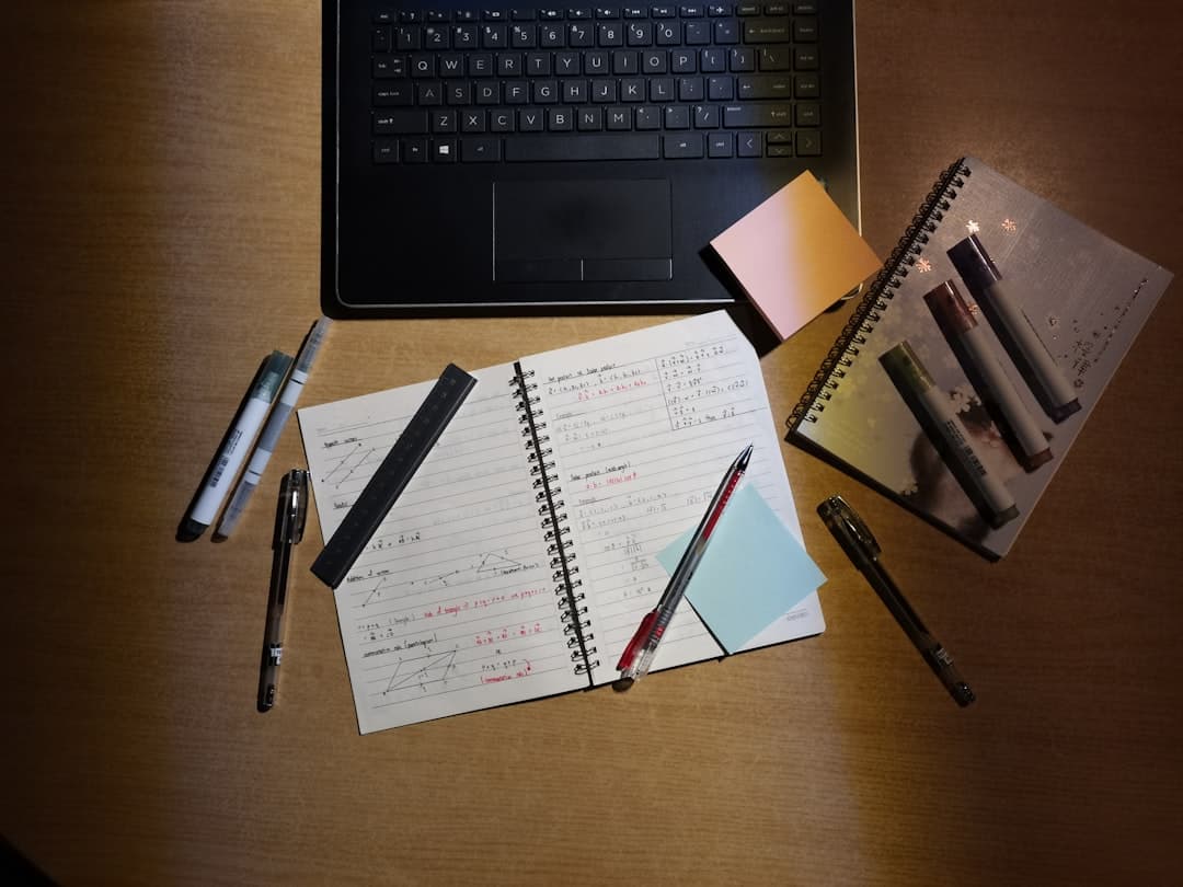 Faceless creator's desk with laptop, notebook, and markers for content planning and research.