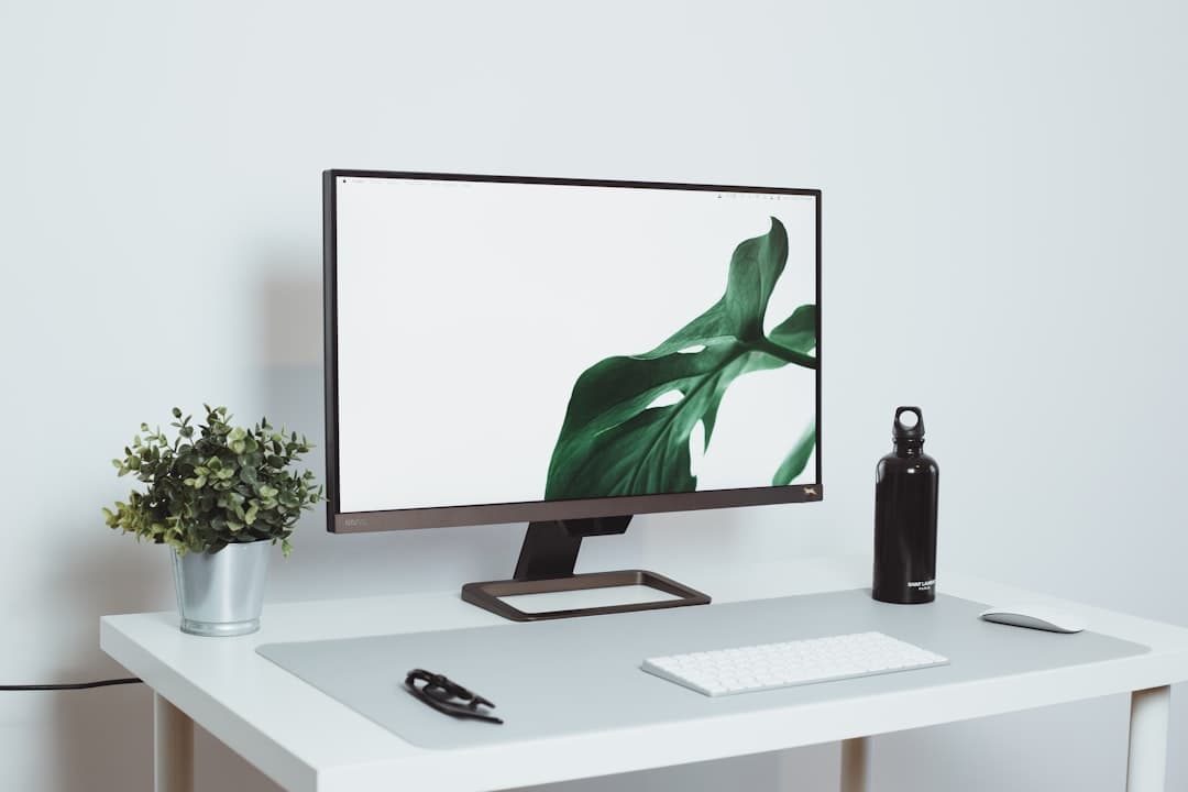 Clean desk with a monitor displaying abstract green leaves, keyboard, mouse, and water bottle.