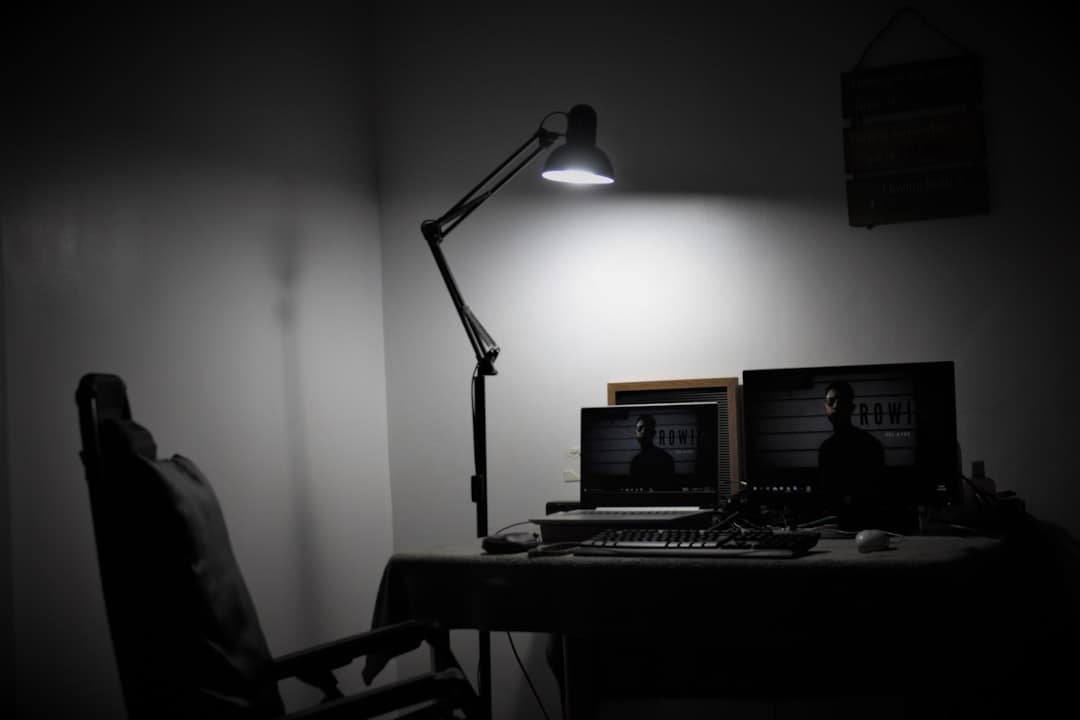 Dark home studio desk with two monitors displaying video content and a desk lamp.