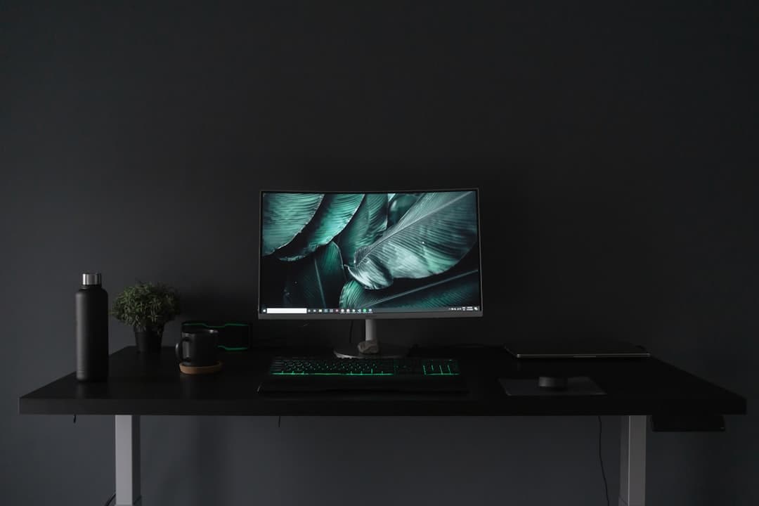 Clean desk setup with a curved monitor displaying nature art, keyboard, and water bottle for faceless YouTube content creation.
