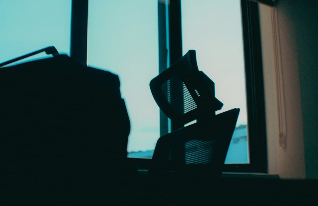 Silhouette of an empty office chair and desk with a large window in the background, suggesting a creator's workspace.
