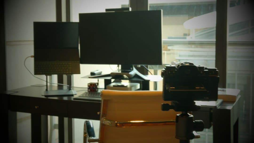 Faceless YouTube creator's desk with dual monitors, camera, and keyboard for content ideation.